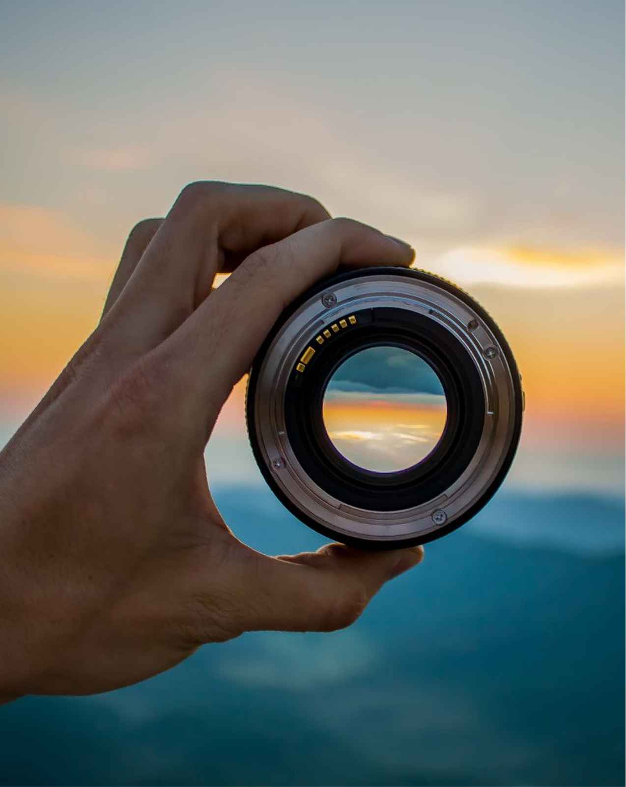 Hand holding a camera lens that reflects the horizon at sunset